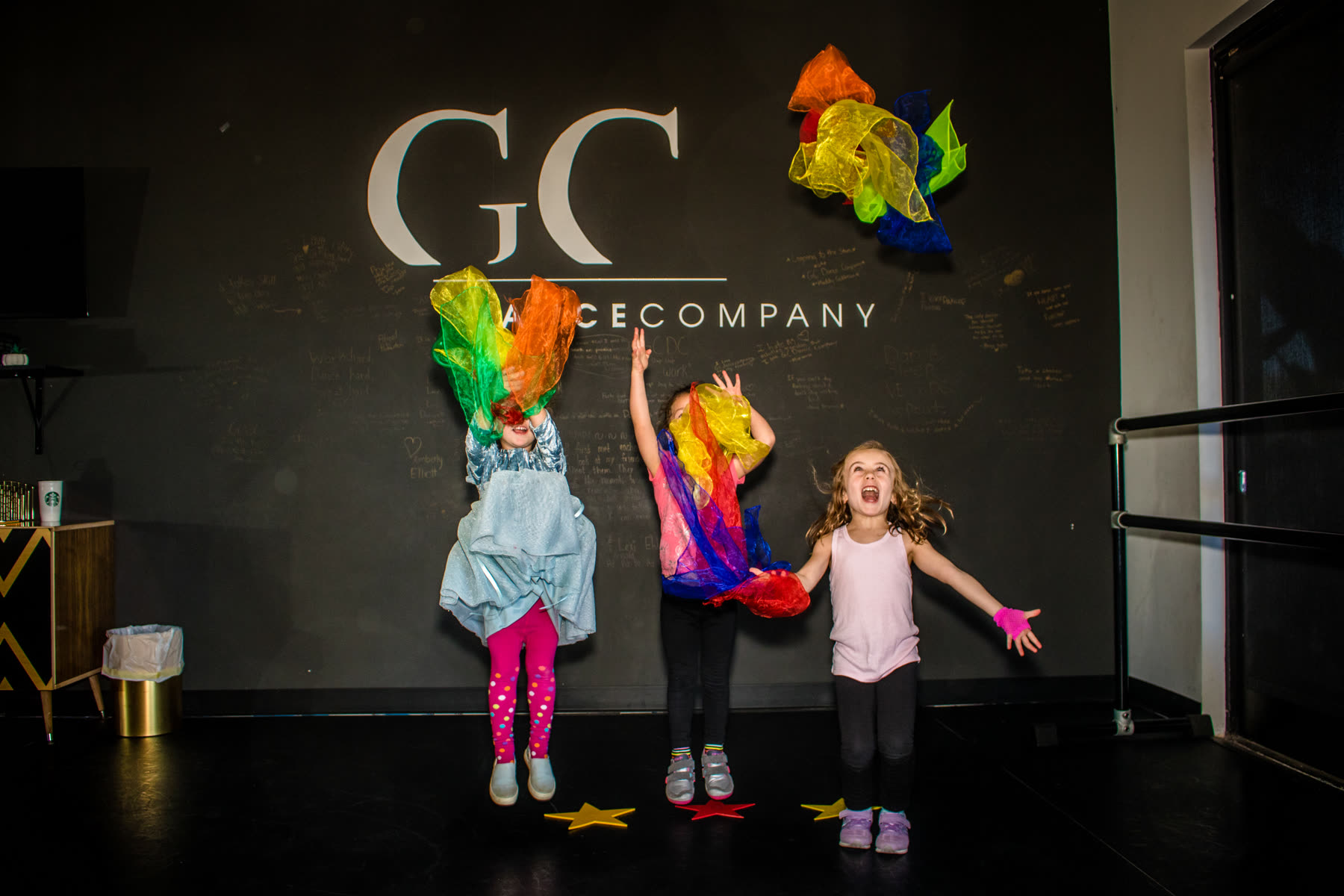 Two young dancers in rainbow tutus posing in front of the GC Dance Company wall