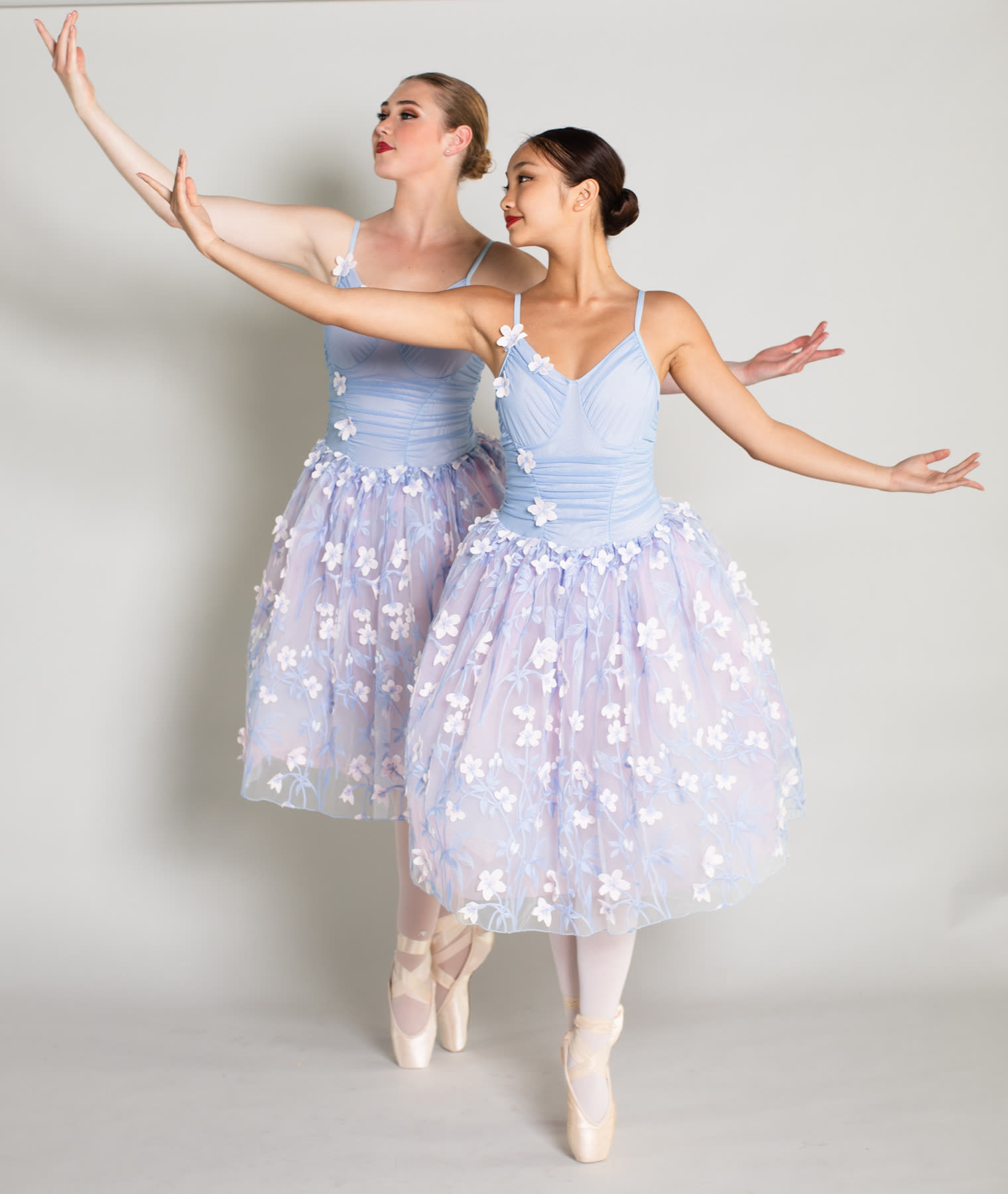 Two young ballerinas in lilac tutus, arms raised