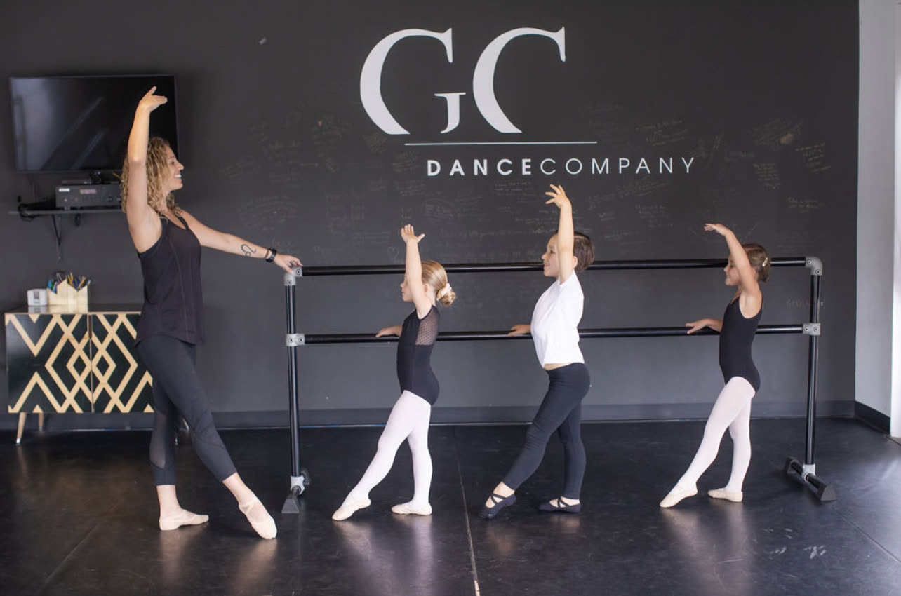 Students at the barre in the studio, beneath the GC Dance Company sign